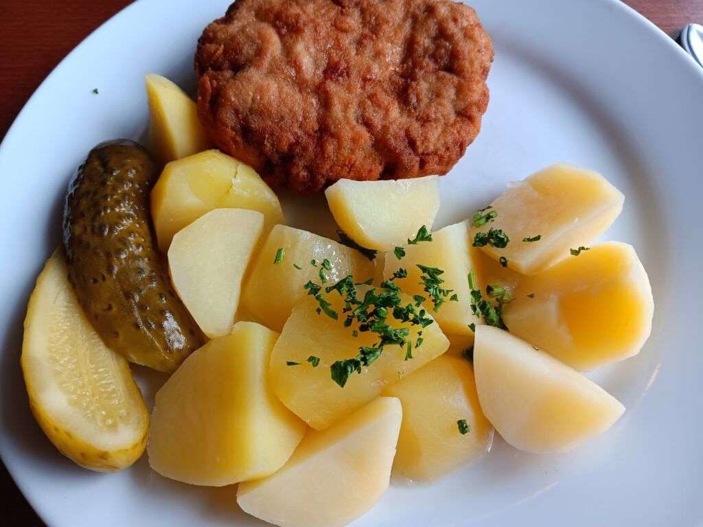 Smažený řízek z mletého vepřového masa obalený v trojobalu podávaný s vařeným bramborem a kyselou okurkou